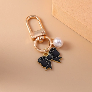 Elegant gold keychain with a black enamel bow and a white pearl charm for bags