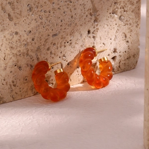 Détail macro de boucles d'oreilles torsadées en acrylique ambre avec clous dorés sur pierre