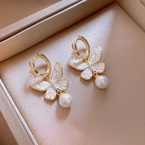 Macro shot of gold butterfly earrings with white enamel and dangling pearls in a box