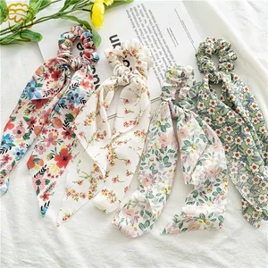 Flat lay detail of four floral chiffon hair scrunchies with long ribbons on white fabric