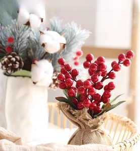 Close-up of artificial red berry branches with green leaves in a burlap base