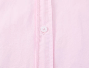Close-up of light pink poplin shirt showing clean stitching and white button detail