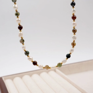 Colorful gemstone and freshwater pearl necklace with gold accents on beige jewelry tray