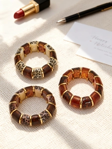 Detail view of 18k gold plated leopard resin bangles on a textured beige fabric background