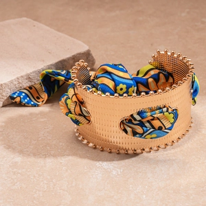Detail of gold metal cuff bracelet with colorful silk scarf wrap and textured finish