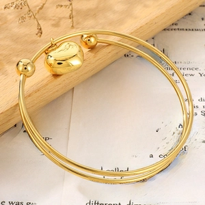Detail shot of a golden double-loop bangle with heart pendant on a rustic wooden tray