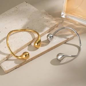 Detailed close-up of polished gold and silver water drop open bangles on stone plates