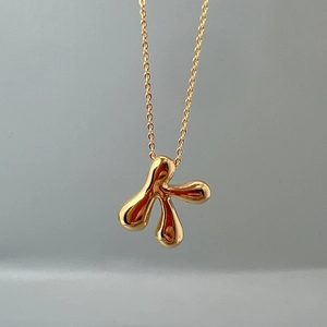 Close-up of golden letter K pendant necklace with polished irregular fluid metal design