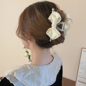 Elegant cream ribbon bow hair claw with rhinestones shown on a bun hairstyle