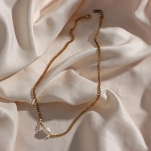 Macro view of 18K gold chain necklace featuring a single freshwater pearl on beige silk