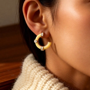 Close-up of C-shape cream enamel earrings with gold accents and sparkling stones on model