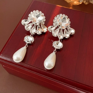 Detailed close-up of floral crystal earrings with teardrop pearls on vintage wood box