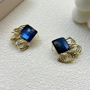 Close-up of deep blue square crystal pendant with golden rings on high-quality earrings