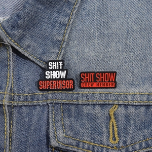 Detail of Shit Show Supervisor and Crew Member enamel pins on a blue denim jacket