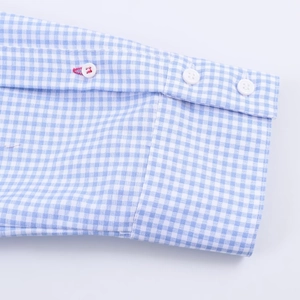 Detail of blue gingham shirt cuff with white buttons and red contrast stitching accents