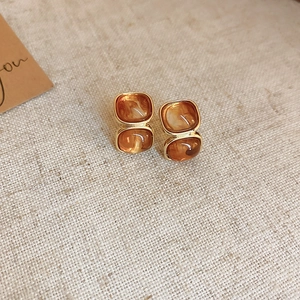 Detailed view of amber resin earrings with gold plating on a textured beige fabric