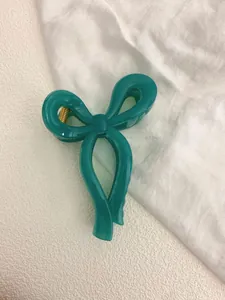 Detail of dark green bow hair claw clip made of polished acrylic with gold spring