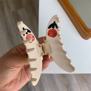 Detail of beige butterfly hair claw clip with red dots on a simple wooden floor