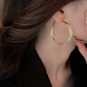 Detail shot of large golden hoop earrings with spiral texture on female model