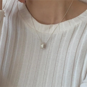 Detail of a 925 sterling silver heart necklace worn with a white knitted top