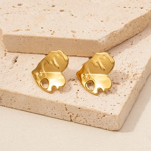 Detail of gold irregular heart-shaped stud earrings on beige porous stone