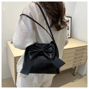 Minimalist black synthetic leather shoulder bag with a large bow detail on a model