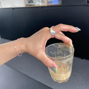 Detail of S925 silver fan-shaped ring and pink beaded bracelet on hand with coffee