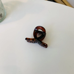 Close-up of tortoise shell resin hair claw clip with crossed twist design on white background