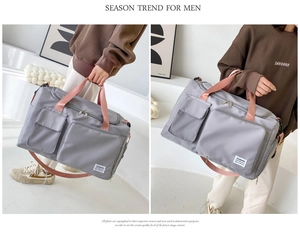 Detail of grey travel bag with pink handles featuring dual front pockets and shoulder strap