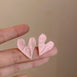 Dettaglio di orecchini a cuore rosa irregolari con finitura metallica ruvida sulla mano