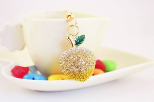 Detail of apple keychain with sparkling rhinestones and green leaves on a cup edge