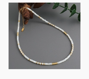 Detailed macro view of a beaded necklace with white square beads and gold brass cylinders