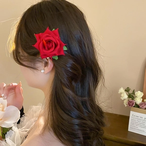 Detail of red fabric rose hair clip with realistic velvet petals on brown wavy hair