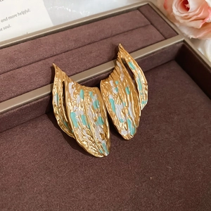 Close-up of golden leaf earrings with turquoise enamel on a brown velvet tray