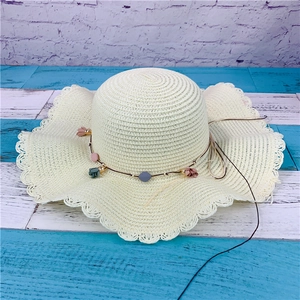 Detail of cream straw hat with woven texture, wavy brim, and decorative floral beaded cord