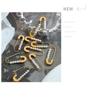 Detail shot of 18K gold plated safety pin earrings with elegant white faux pearls