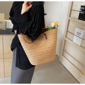 Detail of a large straw tote bag with brown leather straps worn on shoulder