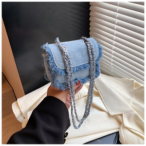 Close-up of light blue denim mini crossbody bag with frayed edges and silver chain strap