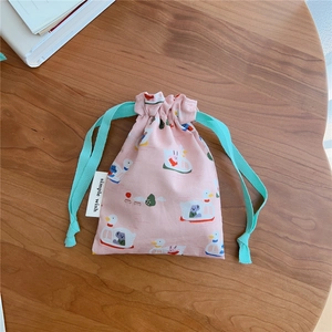 Close-up of pink cotton drawstring bag with duck prints and green rope on a wooden desk