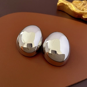 Minimalist silver oval stud earrings with polished mirror finish on brown leather
