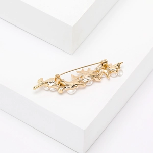 Detail of a gold-plated branch brooch with white pearls on a minimalist display stand