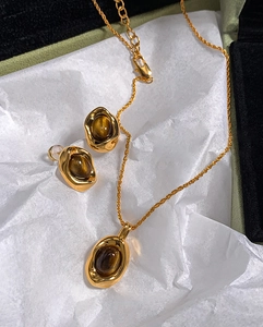 Detail of gold-plated necklace and earrings set featuring oval tiger eye stones