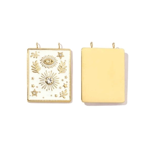 Macro detail of gold-plated rectangular charm with white enamel and evil eye pattern