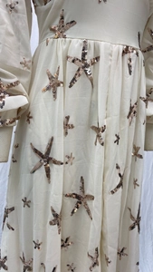 Close-up of gold starfish sequins on a cream chiffon dress with lantern sleeves