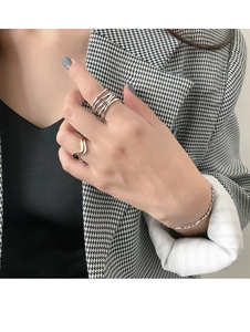 Detailed view of stacked silver wavy rings and a twisted gold bracelet on a model