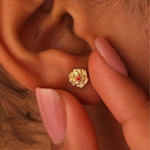Minimalist gold flower stud earrings with red crystal stone on model's ear