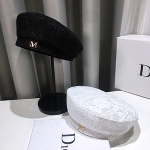 Detail of lace beret showing intricate floral mesh patterns and metallic M letter accent