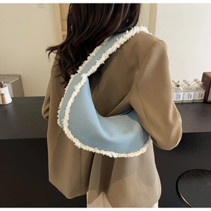 Blue denim crescent shoulder bag with white faux shearling fringe detail on a model