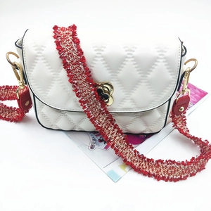 Close-up of white quilted leather bag with floral gold clasp and red woven tassel strap