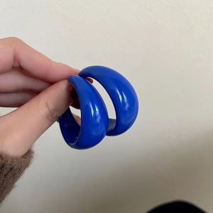 Close-up of blue acrylic C-shaped hoop earrings with a glossy finish and smooth texture